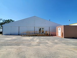 White commercial tent with central entrance and ramp access, set up on a concrete lot for an event or temporary workspace.