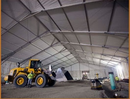  Interior of an expansive industrial tent with a yellow front loader moving materials, illustrating an active construction environment.